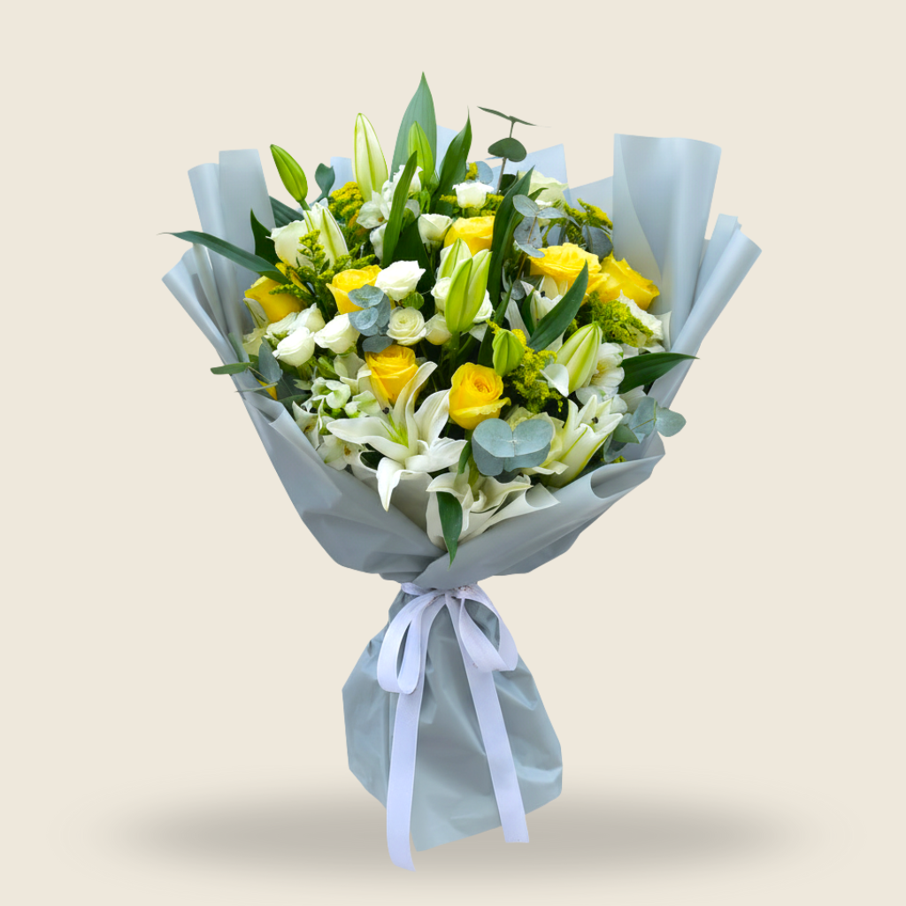 Large bouquet of white lilies, yellow roses, and greenery wrapped in grey paper