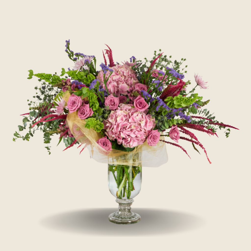 Grand vase arrangement of pink hydrangeas, roses, and lush greens with gold mesh